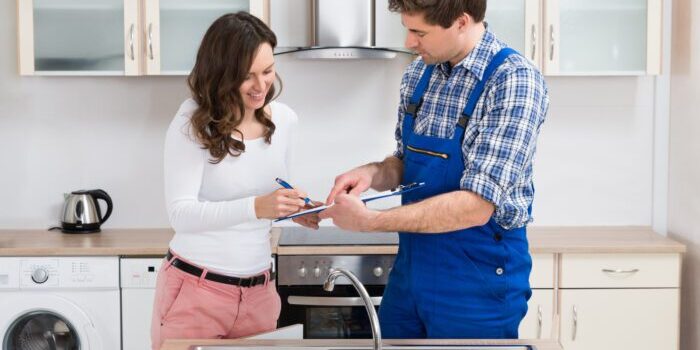 Woman Writing On Clipboard With Plumber In Kitchen Room Happy Woman Writing On Clipboard With Male Plumber Standing In Kitchen Room